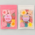 Three resealable stand-up pouches of colorful candy party favors displayed side by side on a light gray background, with pink and lavender header and footer banners reading 'Hen Party Favourites' and 'Large Size 15 x 10 cm'. The pouches contain assorted flower and heart-shaped candies, and the labels show custom hen party text including 'Bachelorette's Hen Party' and 'Team Hen'.